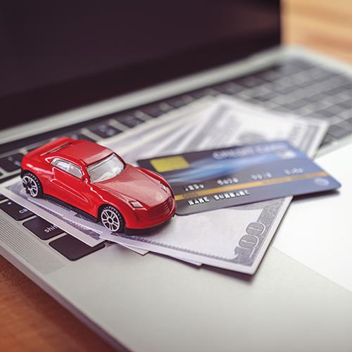 A Red Toy Car Sits on Top of a Laptop with a Credit Card, Showcasing the Potential to Pay Car Loan with Credit Card