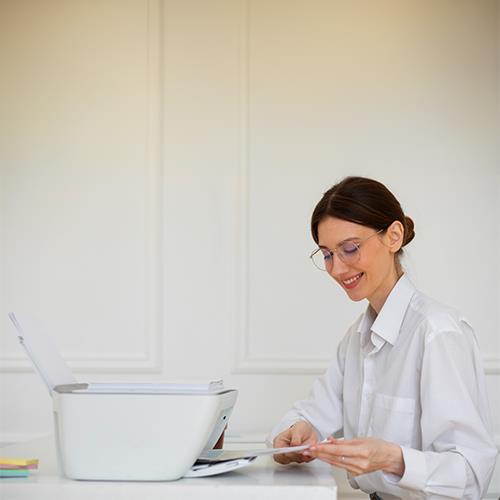 Smiling Professional Woman with Glasses Organizing Documents at Work, with Laptop and Printer in Background and Check Generator.