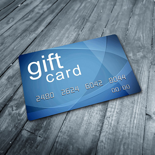 Blue Gift Card with Bold White Lettering at an Angle on a Gray Wooden Surface Depicting Gift Cards Online.