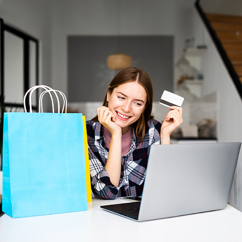 A Woman Enjoying Online Shopping with Credit Card, Sitting at a Laptop Surrounded by Colorful Shopping Bags.