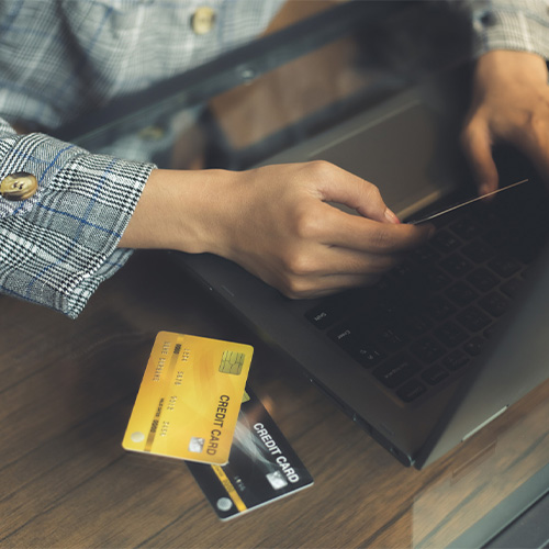 A Person Managing Finances and Making a Payment With Credit Card, Holding It in Hand in Front of an Open Laptop on a Wooden Table