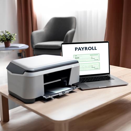 Modern Home Office with a Laptop Showing a Payroll Check Screen Beside an All-In-One Printer on a Wooden Desk.