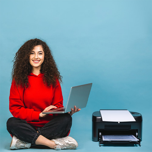 A Woman with Curly Hair Using a Laptop to Write Checks Online, Seated Next to the Printer on the Floor