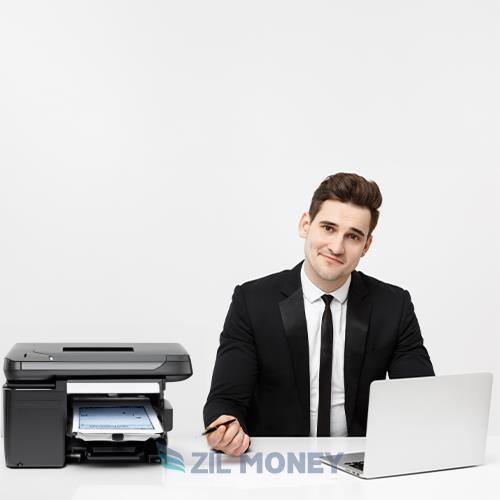 A Young Professional from Check Printing Companies Confidently Sits at a Desk with a Laptop and Printer.