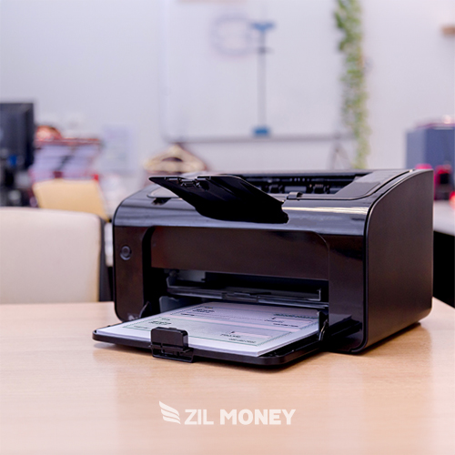 A Black Printer on a Desk Print Business Checks At Home, with the Platform Logo Visible on the Checks. the Office Setting Is Slightly Blurred in the Background