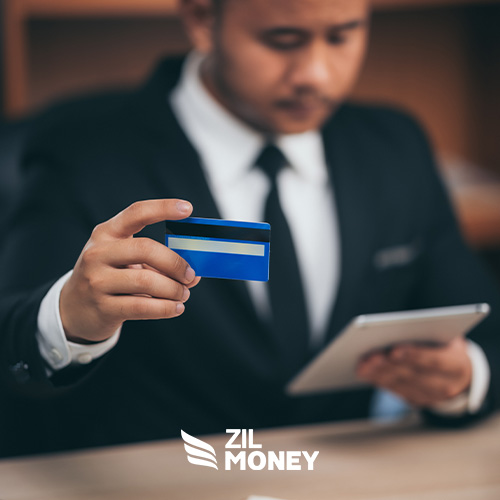 A Businessman Holding a Credit Card While Looking at a Digital Tablet, Exploring Credit Card Processing for Small Business and Earning Cash Back Rewards.