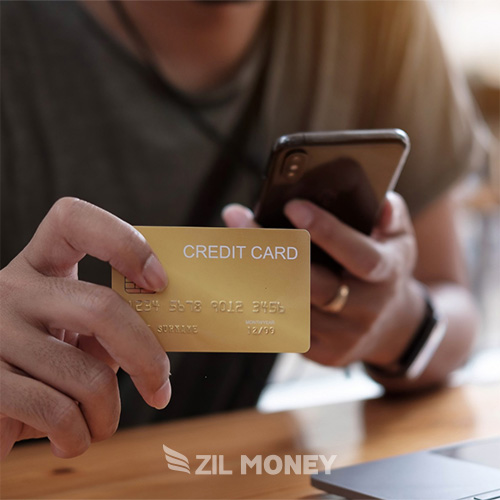 A Man Holding a Credit Card While Looking at a Smartphone, Simplify Payments with Credit Card Processing Services and Earning Cash Back Rewards.