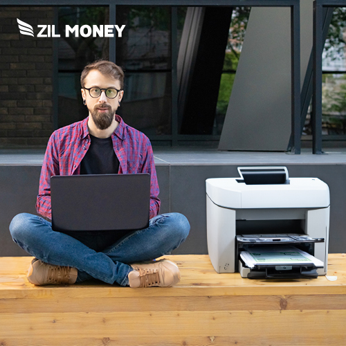 A Man Sitting Near by A Printer With A Laptop Simplifying Your Finances How Check Writing Can Help. Create And Print Checks, Send eChecks, Mail Checks
