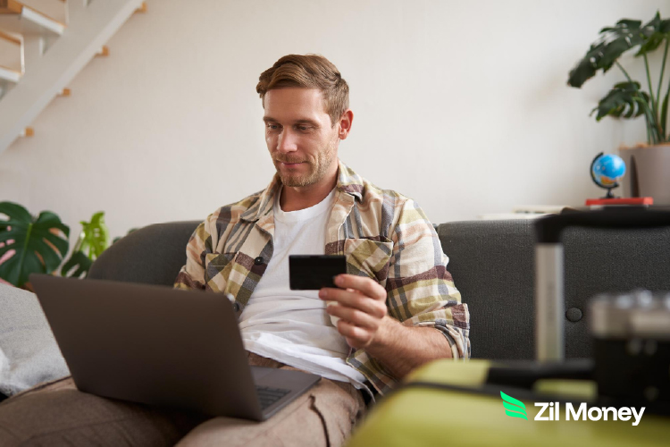 A man using a laptop to make a rent payment with a credit card from his sofa, highlighting the ease of online transactions.