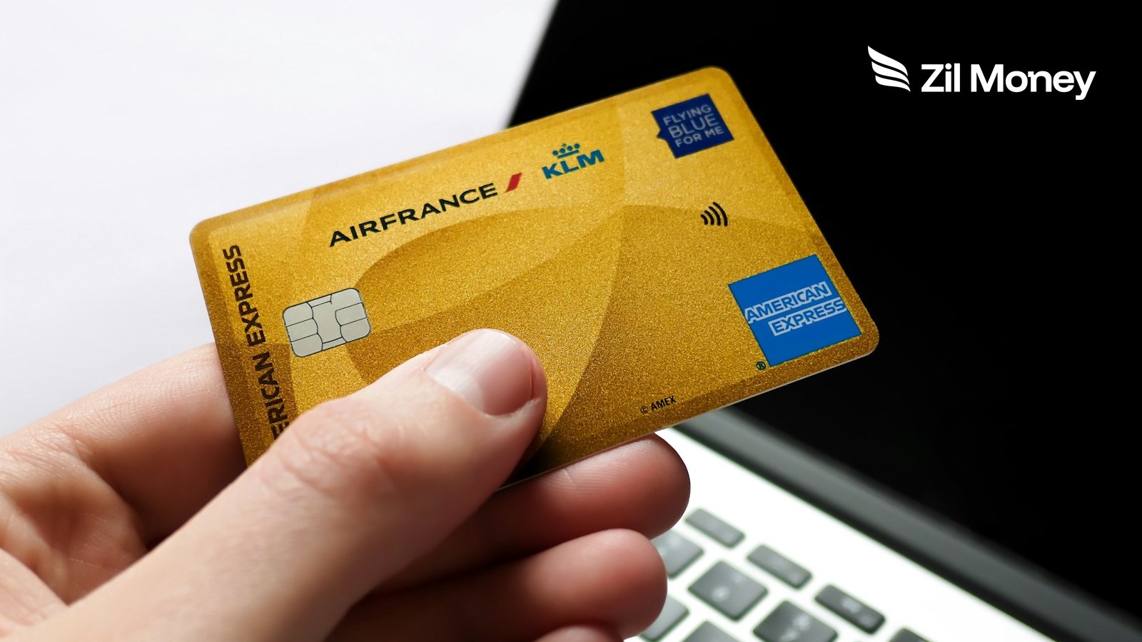 Hand holding an American Express credit card near a laptop to pay business bills with Zil Money