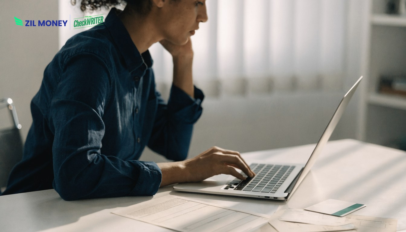 Business owner using a laptop to pay business bills online with invoices on the desk