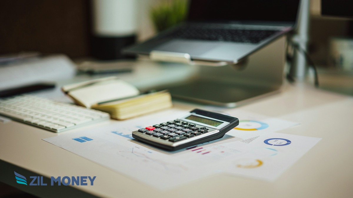 Calculator, notebook, and laptop on a desk with the Zil Money logo, representing choosing the best business credit card for payroll