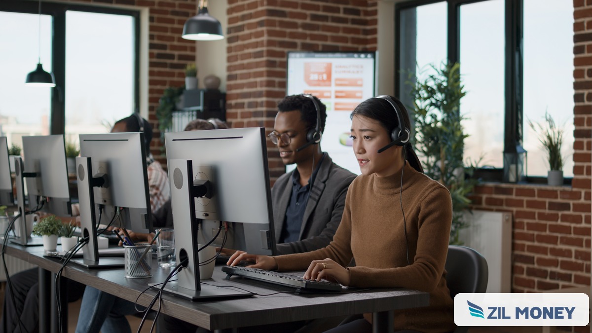 Call center agents at a multi-monitor workstation, with the Zil Money logo in the corner, representing call center payment processing