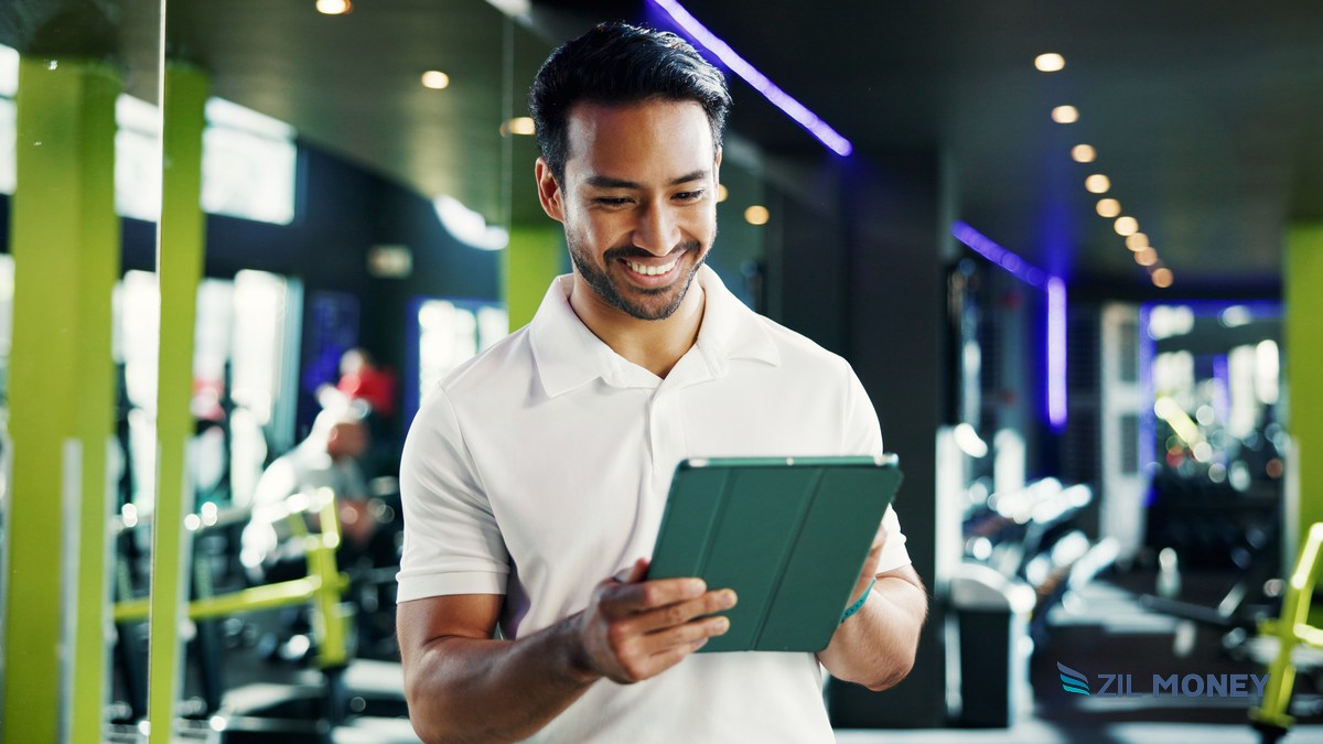 Fitness studio manager reviewing membership dues on a tablet Fitness studio manager smiling while reviewing membership dues collection on a tablet in a gym